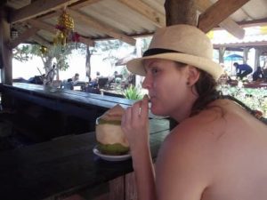 Thailand. Meine Tochter sitzt an einer Beachbar mit Sonnenhut und trinkt aus einer Kokosnus mit Strohhalm. Im Hintergrund Meer